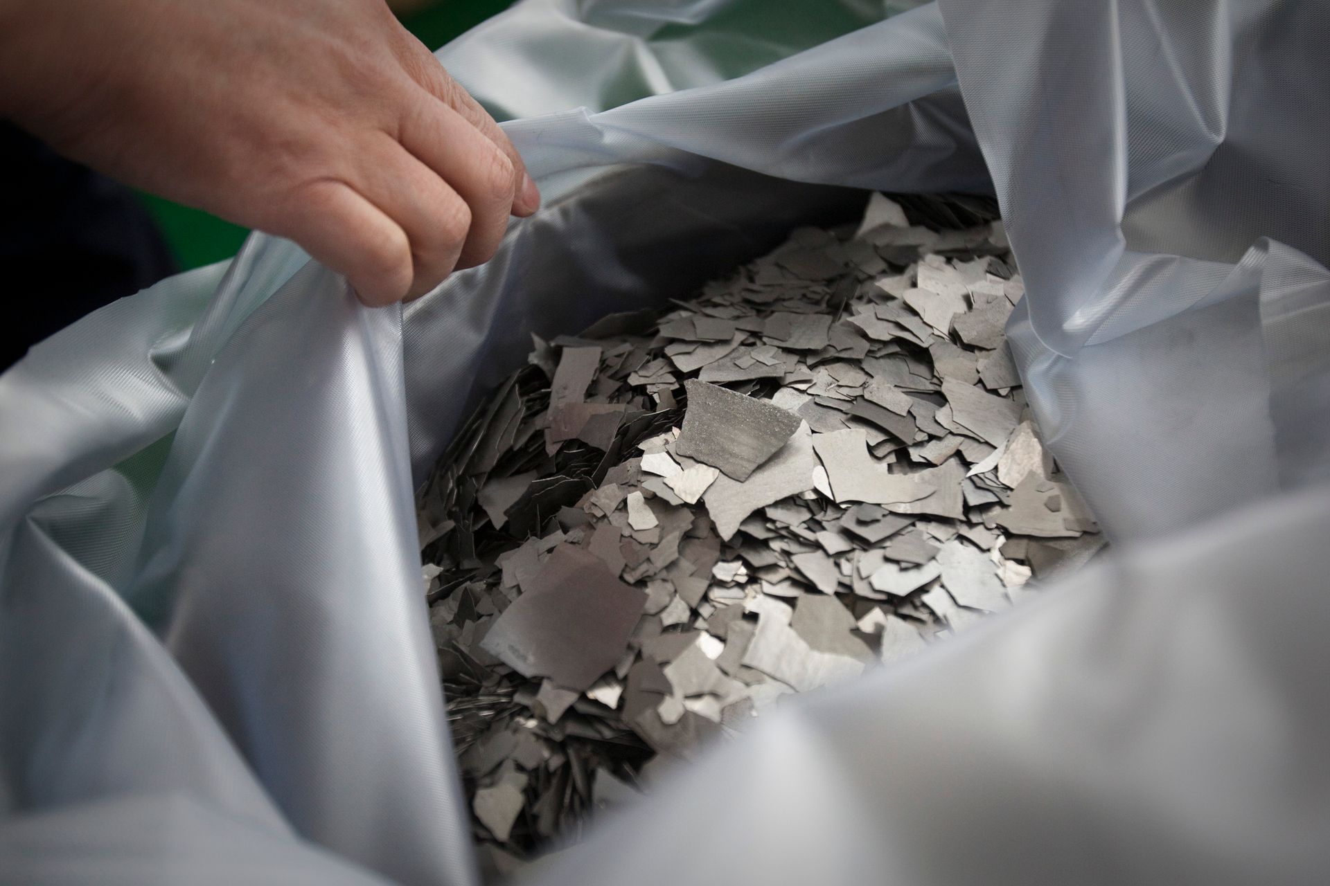 a hand peels back a plastic covering to show pieces of a silver metal