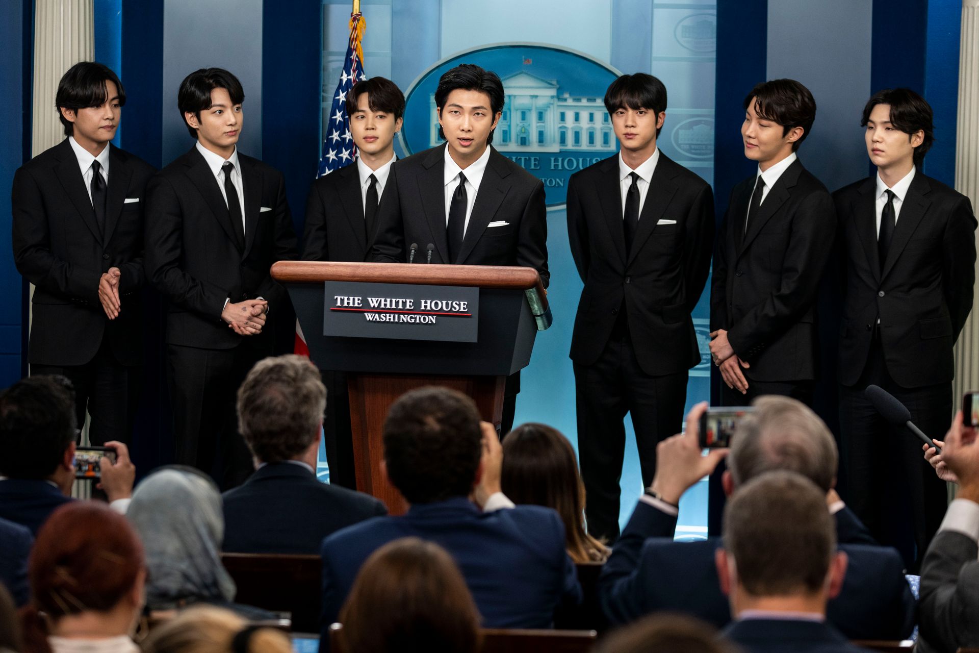 Seven members of BTS stand behind a podium in the White House briefing room