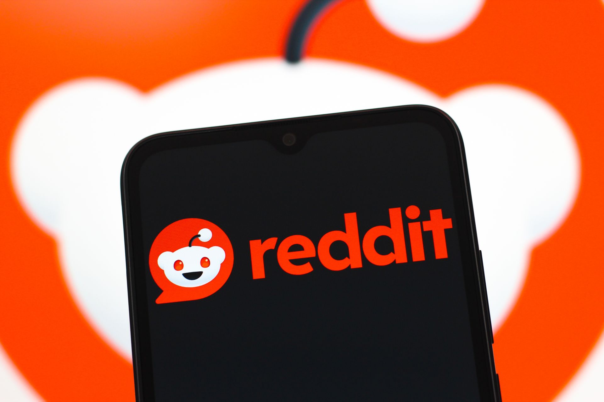 phone showing Reddit's logo on a black screen in front of an image of its logo