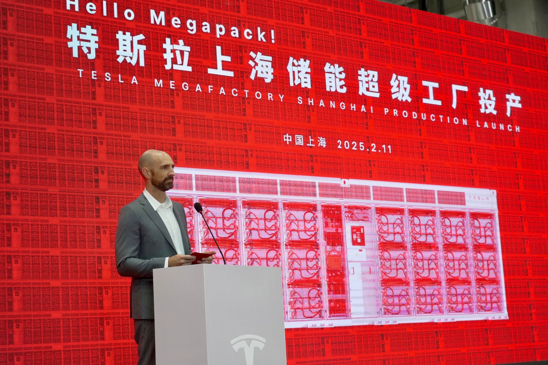 a Tesla VP stands in front of a red screen with Chinese characters and a sign that says "Hello, Megapack" in English