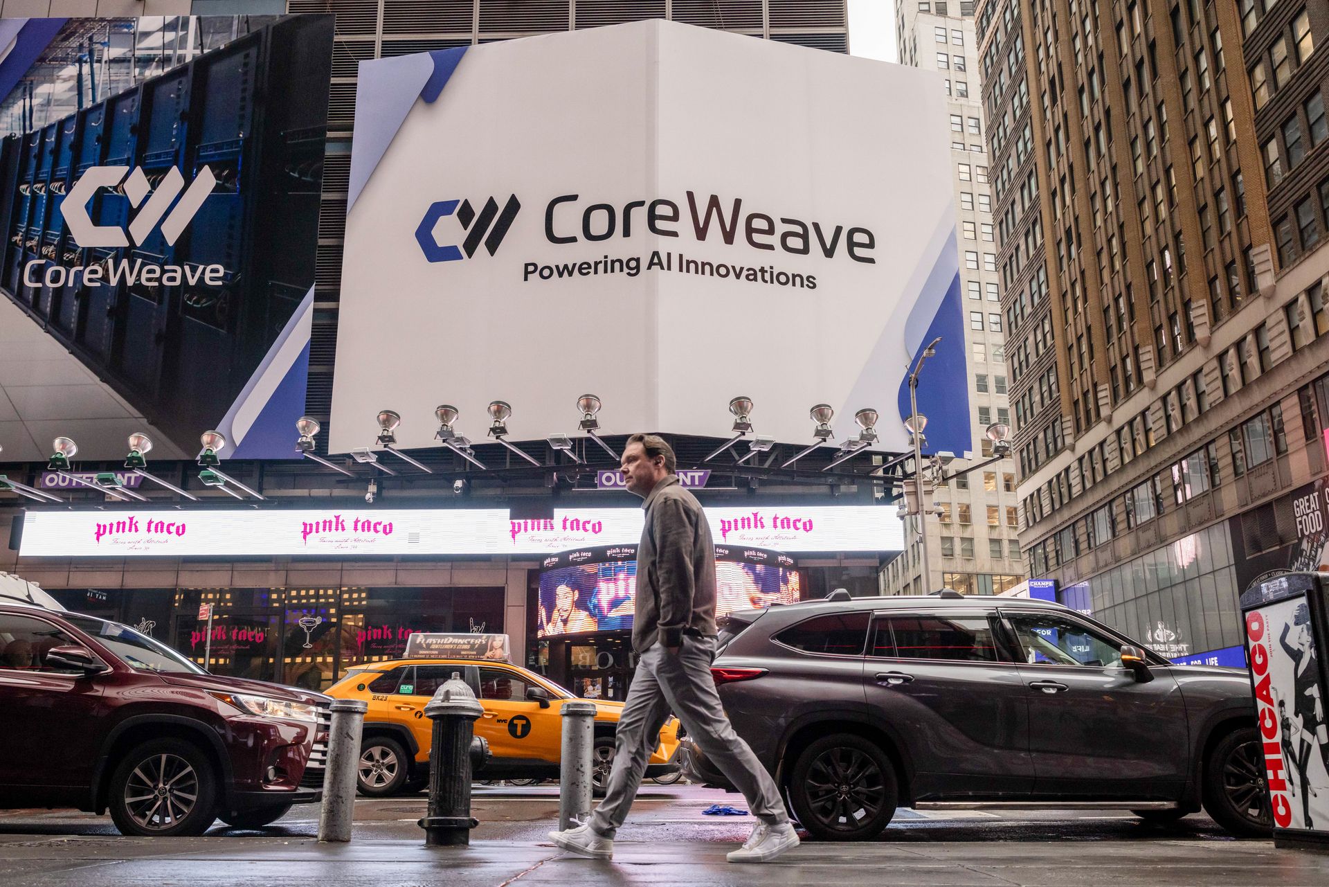 a CoreWeave billboard in New York City where pedestrians, taxis, and cars pass underneath