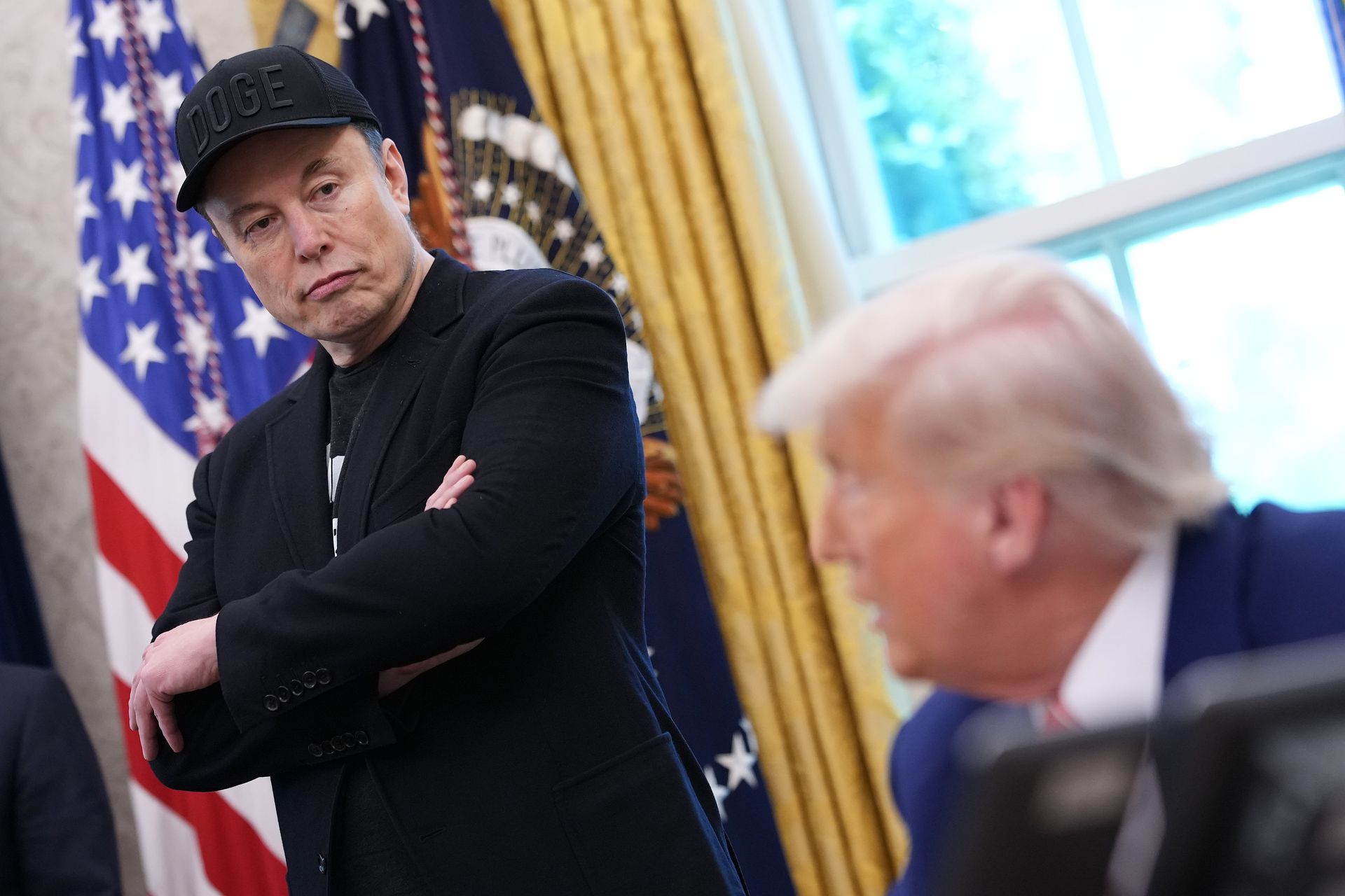Elon Musk and Donald Trump look at each other in the Oval Office