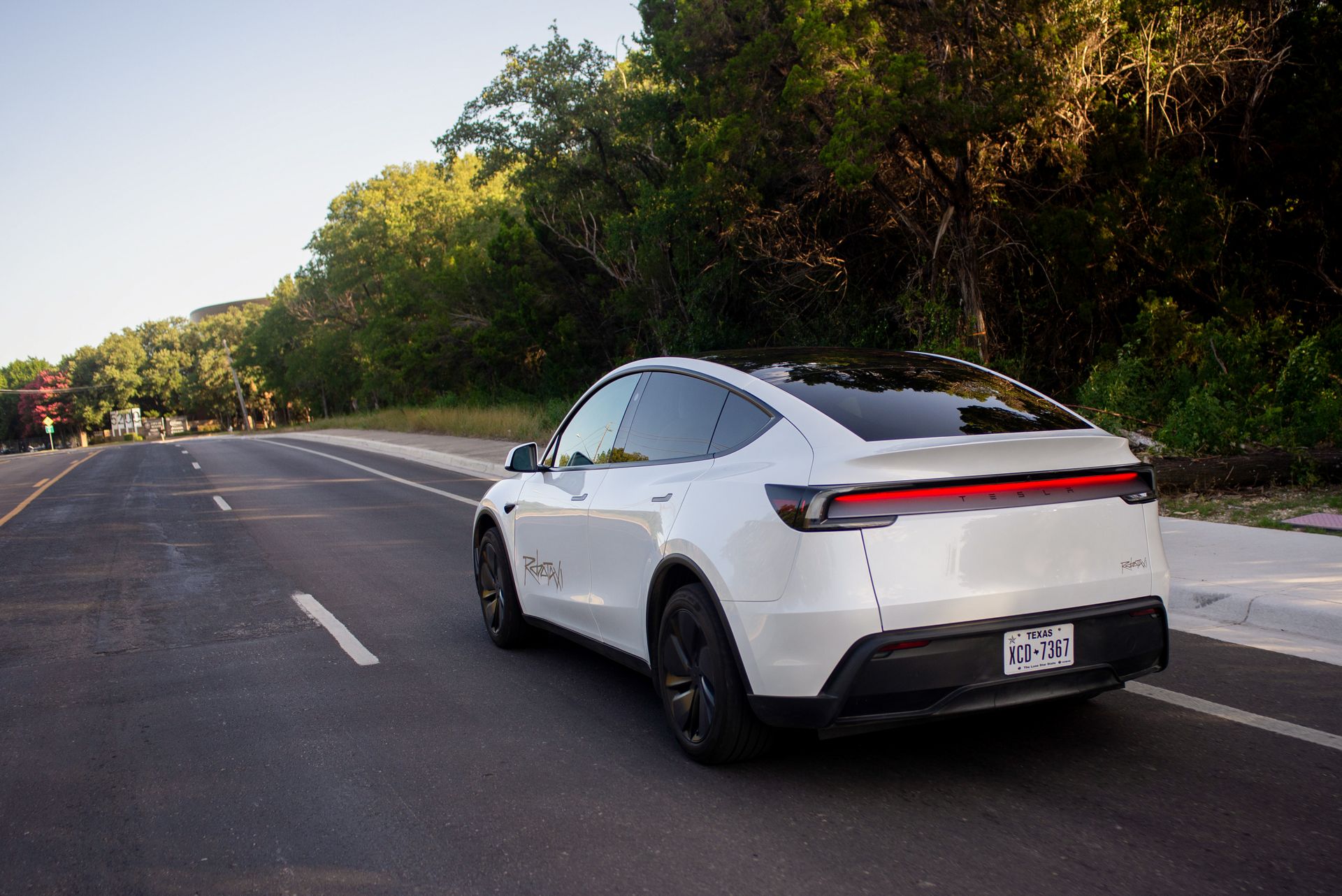a white Tesla robotaxi drives away on a road