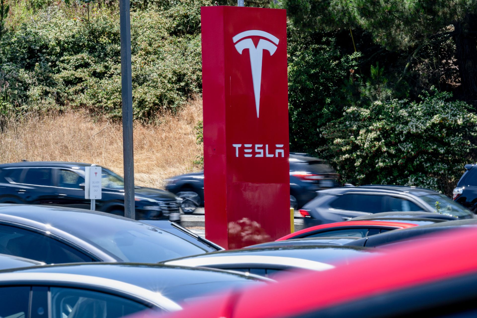 Tesla cars on a lot in front of a red Tesla sign with the logo