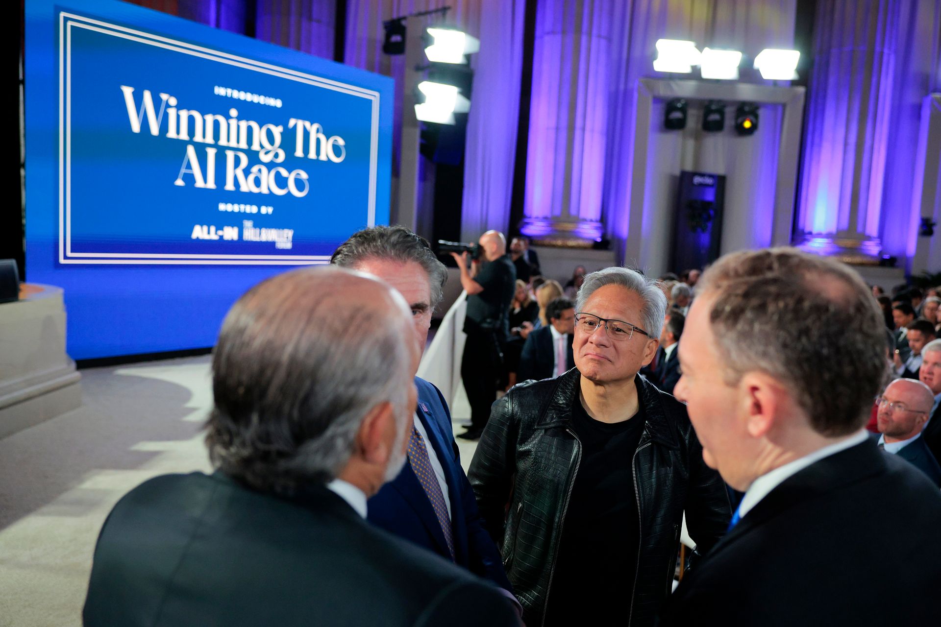 Nvidia CEO Jensen Huang stands in a group of people with "Winning the AI Race" on a screen behind him