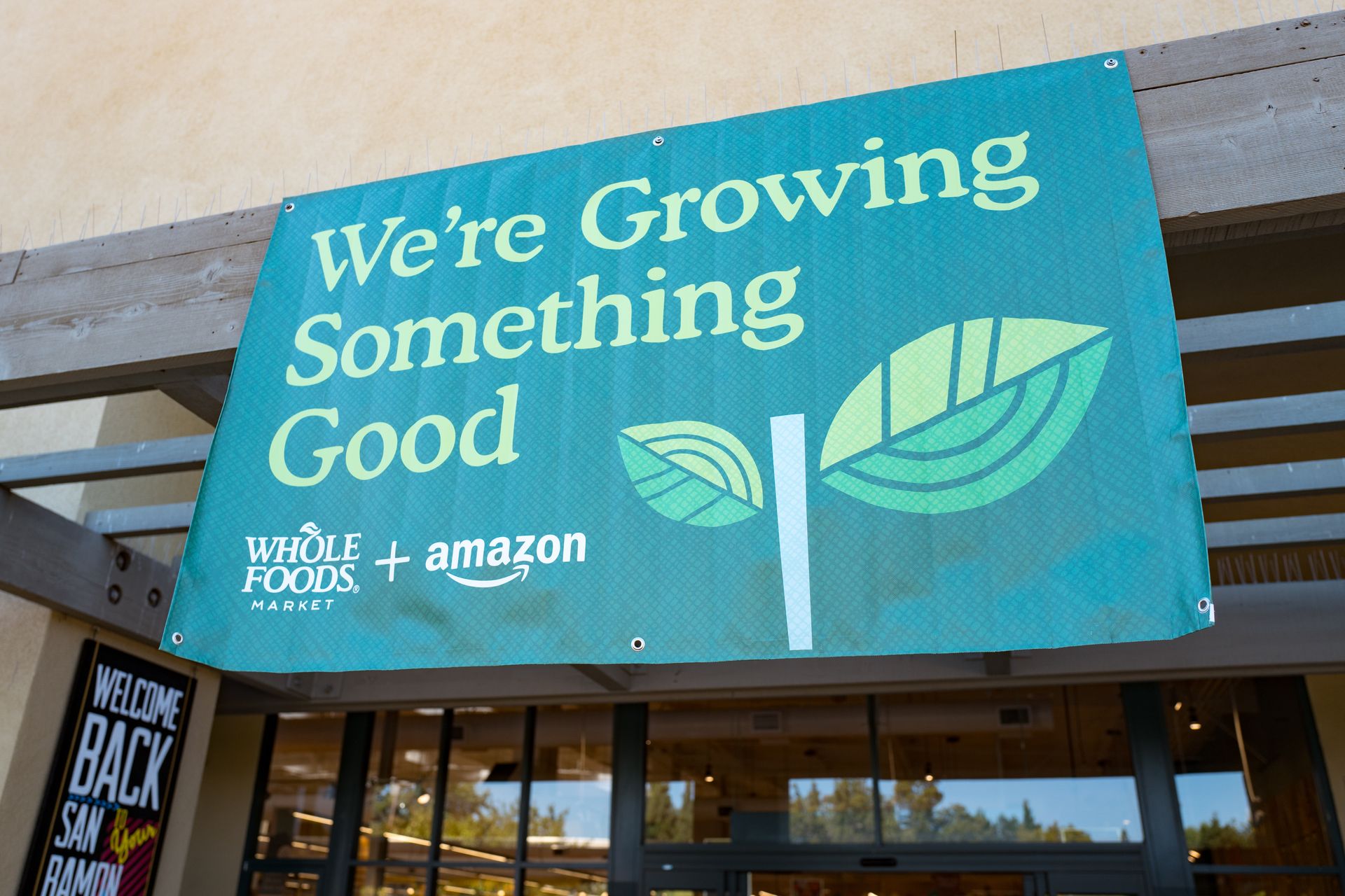 an exterior of a store with a green sign with Whole Foods and Amazon logos that says "We're growing something good"