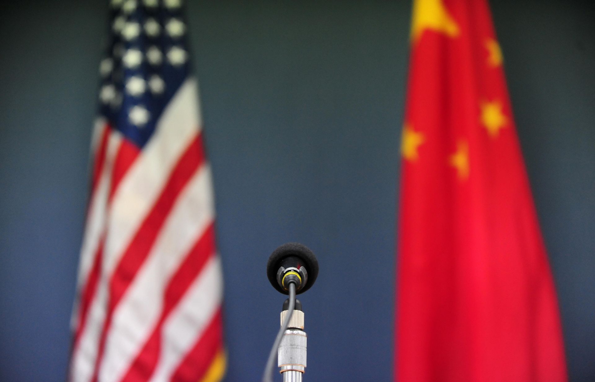 A U.S flag on the left and a Chinese flag on the right sit blurred behind a microphone on a podium in the center